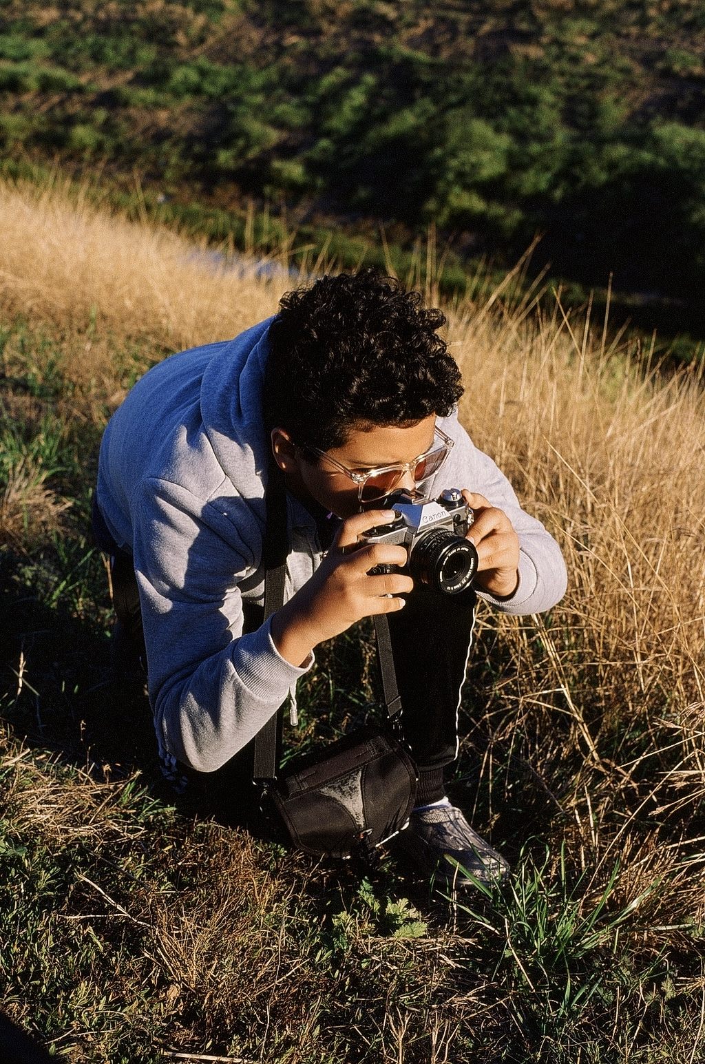Young photographer crouching in golden grass with a film camera