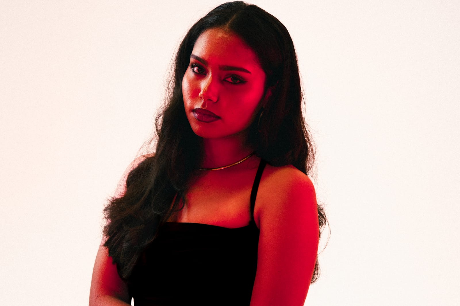 Woman in a black top lit in red against a pale backdrop