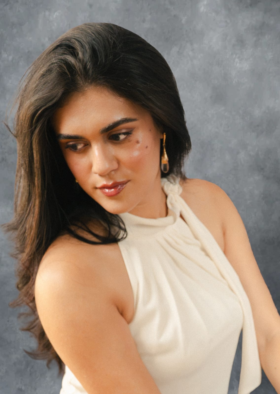 Woman in a white halter top looking down over her shoulder against a painted grey backdrop