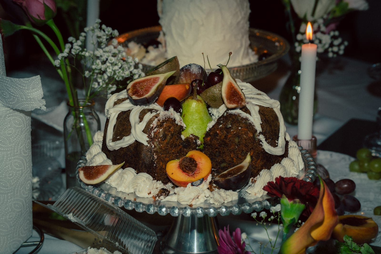 Cake crowned with figs, pears, and apricots on a dessert table by candlelight