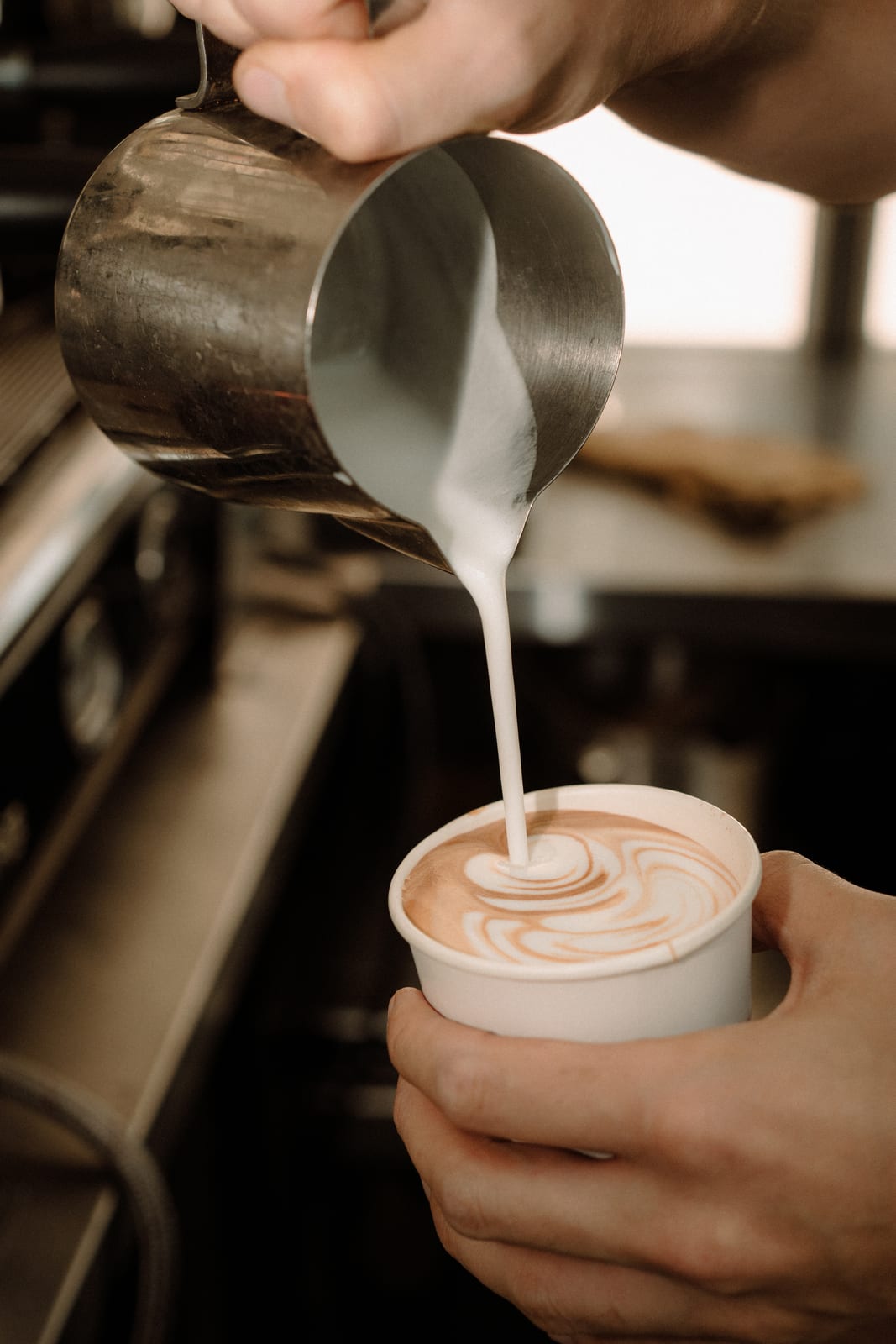 Barista pouring steamed milk into a latte to-go cup