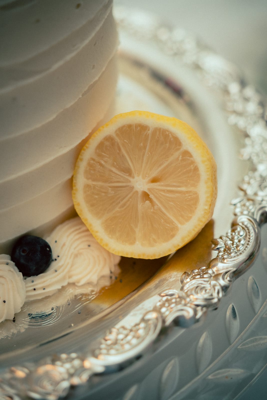 White frosted cake with a lemon slice and blueberry on an ornate silver tray