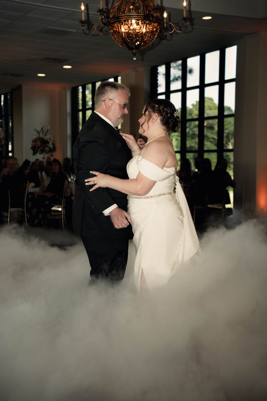Bride and groom dancing in low fog beneath a chandelier