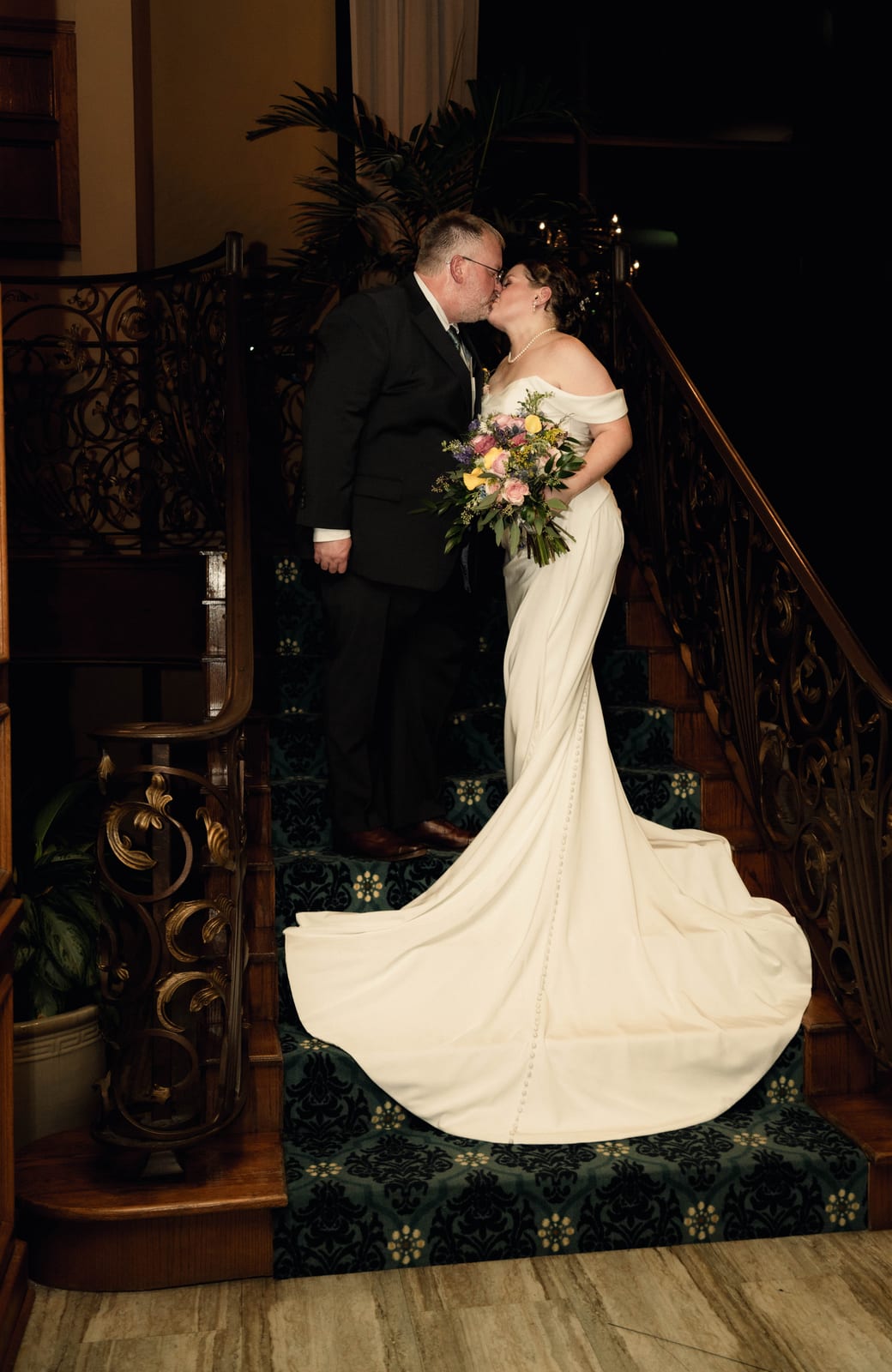 Bride and groom kissing on a carved wooden staircase as her train spills down the steps